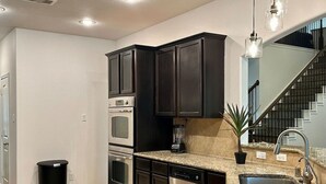 A modern kitchen with dark cabinetry, stainless steel appliances, granite countertops, and a built-in dishwasher. - Beautiful house in The Woodlands - Creekside (Tomball)