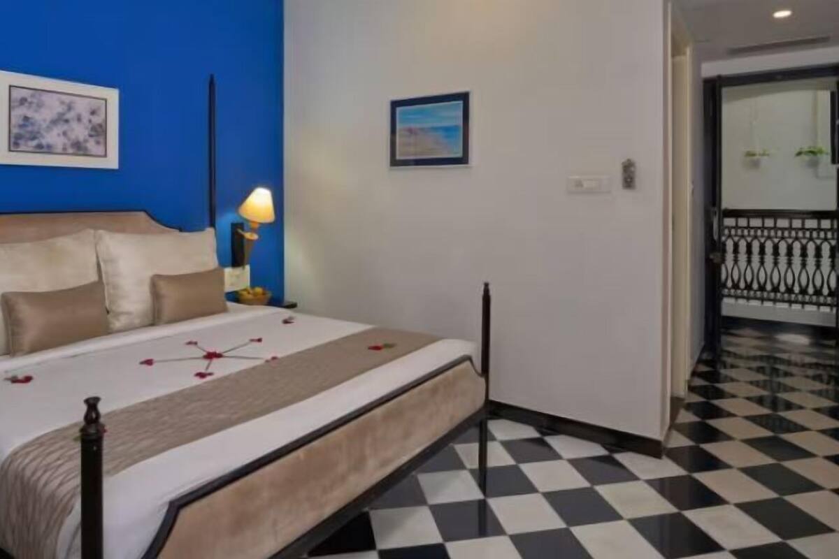 Ein Hotelzimmer mit Schachbrettmuster-Boden, einem Bett mit beigem Kopfteil und zwei Wandlampen.