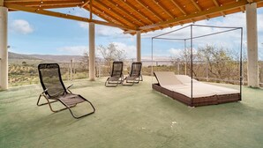 Un patio exterior con una pérgola de madera, una zona de estar cubierta con un toldo y vistas a un paisaje desértico.