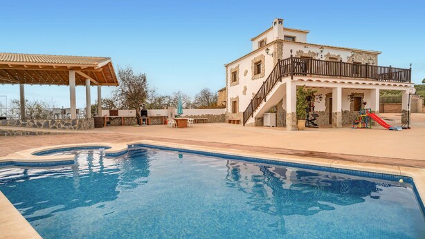 Una piscina con plataforma de piedra, un porche cubierto y un edificio con balc ón y equipamiento de gimnasio al aire libre.
