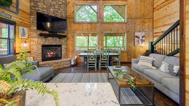 Un salon chaleureux avec une cheminée en pierre, des murs en bois et de grandes fenêtres.
