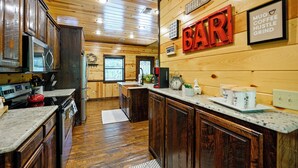 Une cuisine avec des meubles en bois, un réfrigérateur en acier inoxydable et un coin bar agrémenté d’une enseigne indiquant « BAR ».