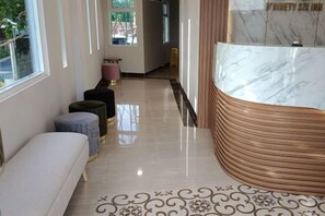A hotel corridor with a bench, ottomans, and a marble reception desk. - D'Ninety Six Inn (Playen)