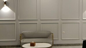 Una stanza con un divano grigio rivestito, un tavolino bianco con piano in marmo e un punto luce a parete.