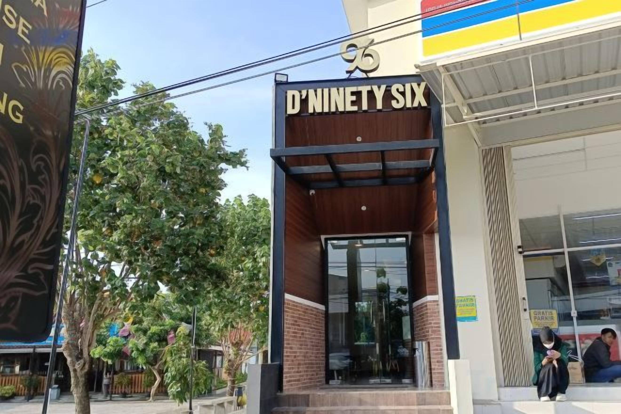 The exterior of D'Neisty Six, featuring a brick facade, large glass entrance, and a clear blue sky.