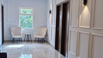 A hallway with two chairs, a small table, and a window with a view of greenery.