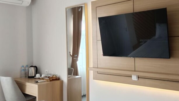 Una camera d'albergo moderna con TV a schermo piatto fissata al muro, una scrivania in legno con una sedia, un letto e uno specchio.