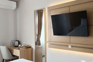 Quarto de hotel moderno com televisão de tela plana na parede, uma escrivaninha de madeira com cadeira, uma cama e um espelho.
