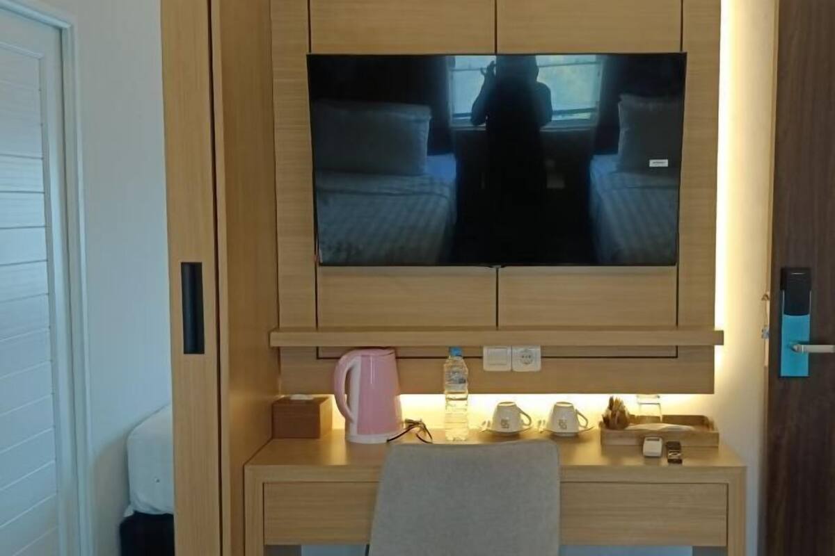 Pieni huone, jossa on sänky, sen yläpuolella seinälle kiinnitetty televisio, pieni työpöytä, jossa on vedenkeitin, vesipullo ja kuppi.