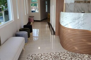 Uma área de recepção de hotel com um balcão de mármore, um banco e um tapete estampado.
