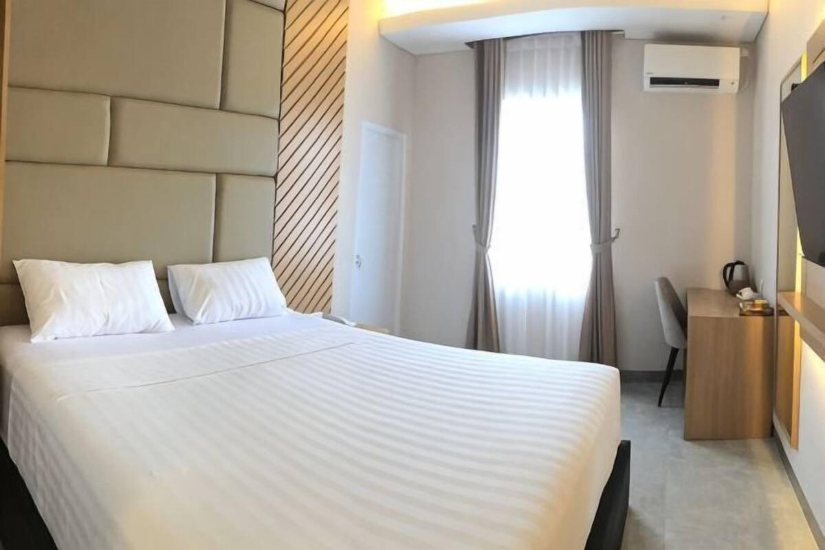 Hotellihuone, jossa on suuri sänky, työpöytä, tuoli, vaatekaappi ja ilmastointilaite.