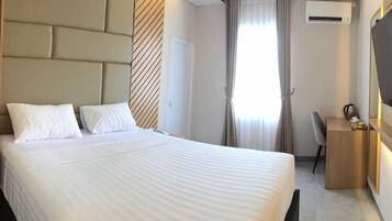 A hotel room with a large bed, a desk, a chair, a wardrobe, and an air conditioning unit.