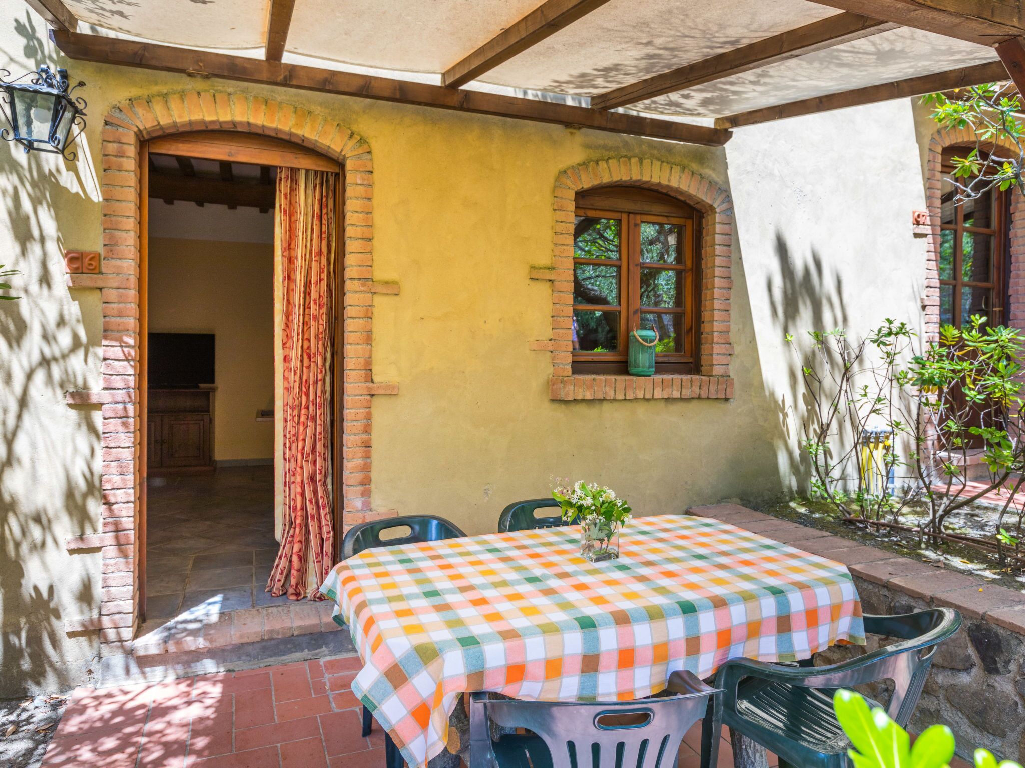 Un patio con una tovaglia a scacchi, due sedie e un tavolino con un vaso di fiori.