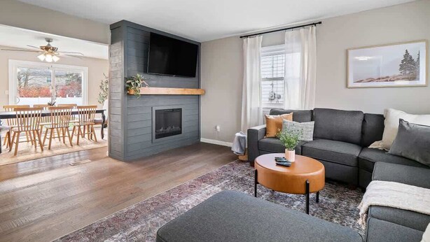 A modern living room with a fireplace, a grey sofa, a coffee table, and a dining area with wooden chairs. - Hot Tub - Game Room - Sleeps 10 - Vermilion (Vermilion)
