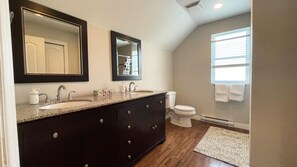 A modern bathroom with a large vanity, double sinks, a toilet, and a window with blinds.