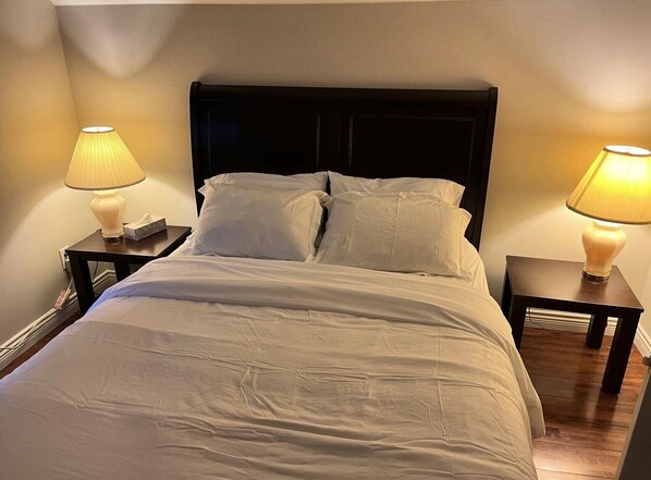 A neatly made bed with white linens, two bedside tables with lamps, and a dark headboard.