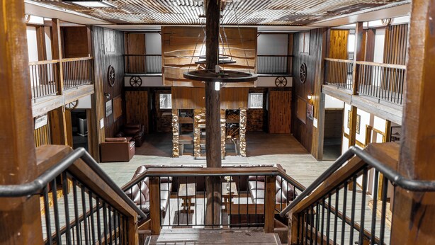 A wooden interior with a central wooden structure, multiple seating areas, and a staircase with wooden railings. - Mount Mee Country Lodge (Mount Mee)