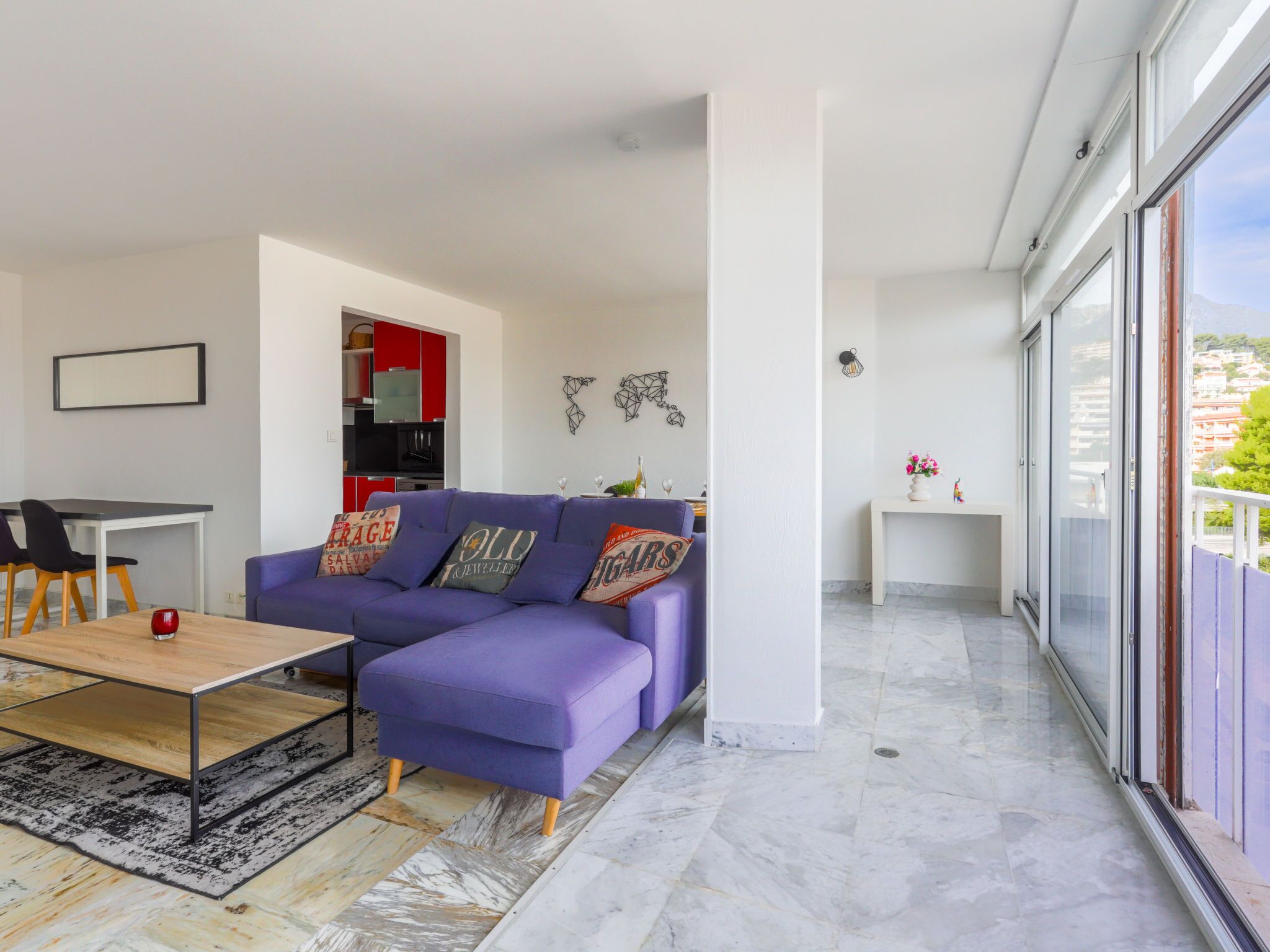 Un salon moderne avec un canapé d’angle violet, une table basse en bois et un coin repas comprenant une table et des chaises blanches.