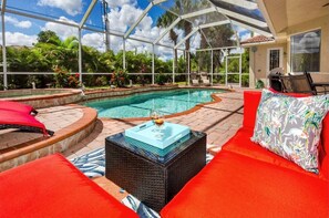 Una piscina exterior techada con sillas de descanso rojas y blancas, una mesa de centro de vidrio y vistas a un paisaje tropical.