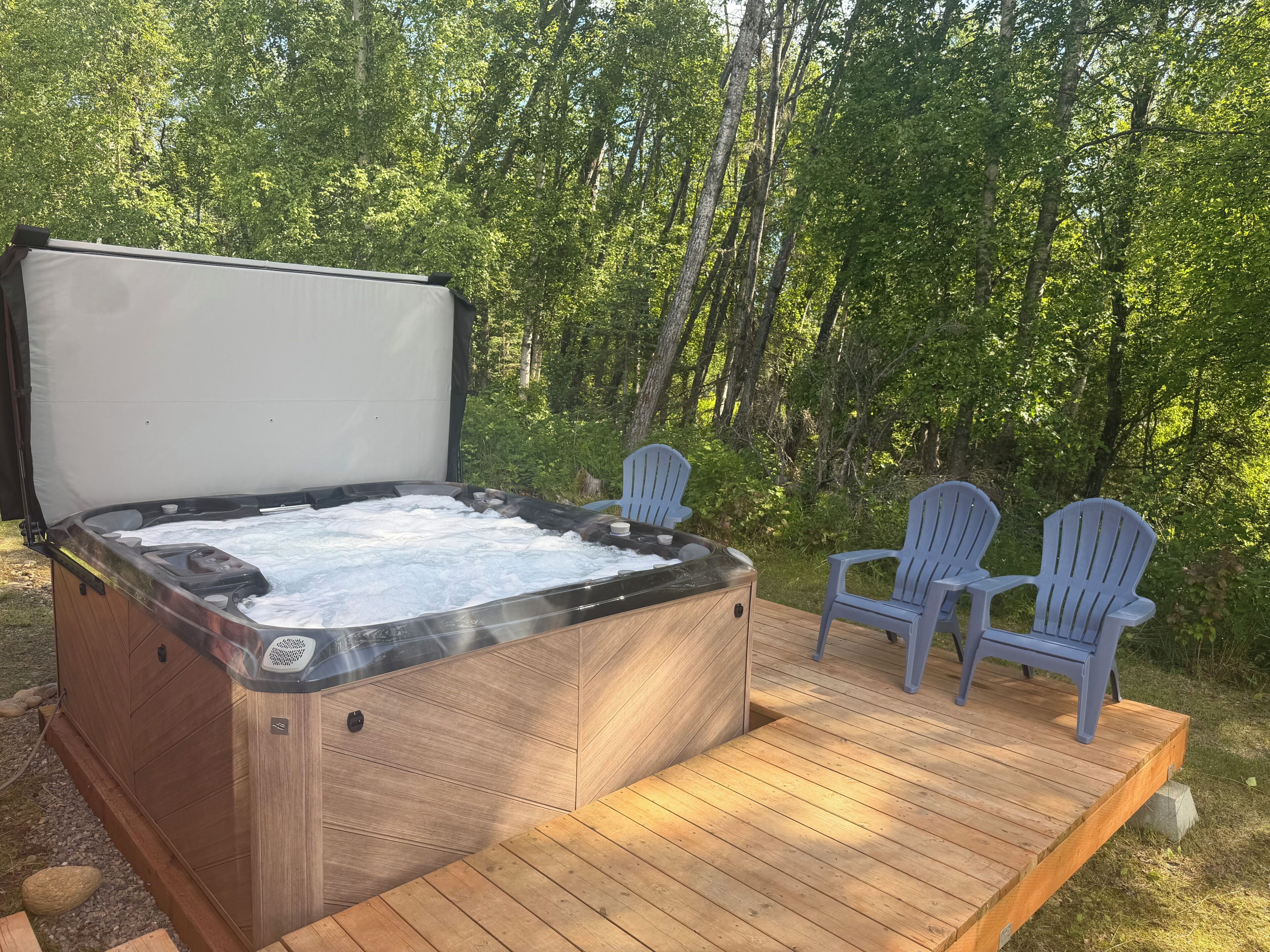 Ein Whirlpool auf einer Holzterrasse mit zwei Adirondack-Stühlen.