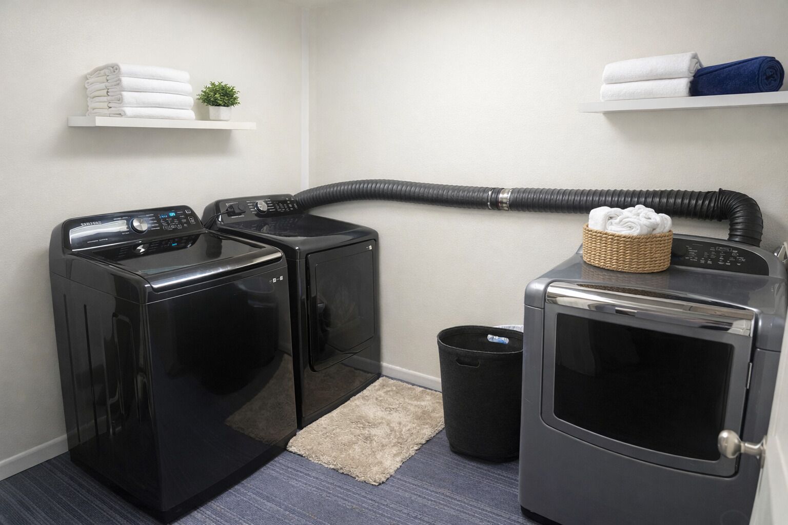 A laundry area with two front-loading washing machines, a dryer, a waste basket, and a shelf with folded towels.