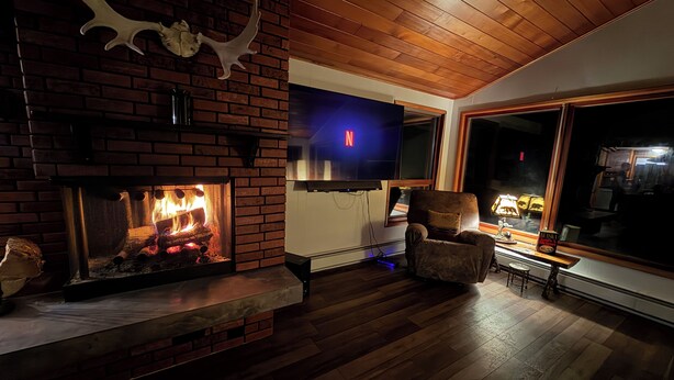 Una sala de estar acogedora con chimenea de ladrillo, un televisor de pantalla plana montado en la pared y un sillón cómodo.