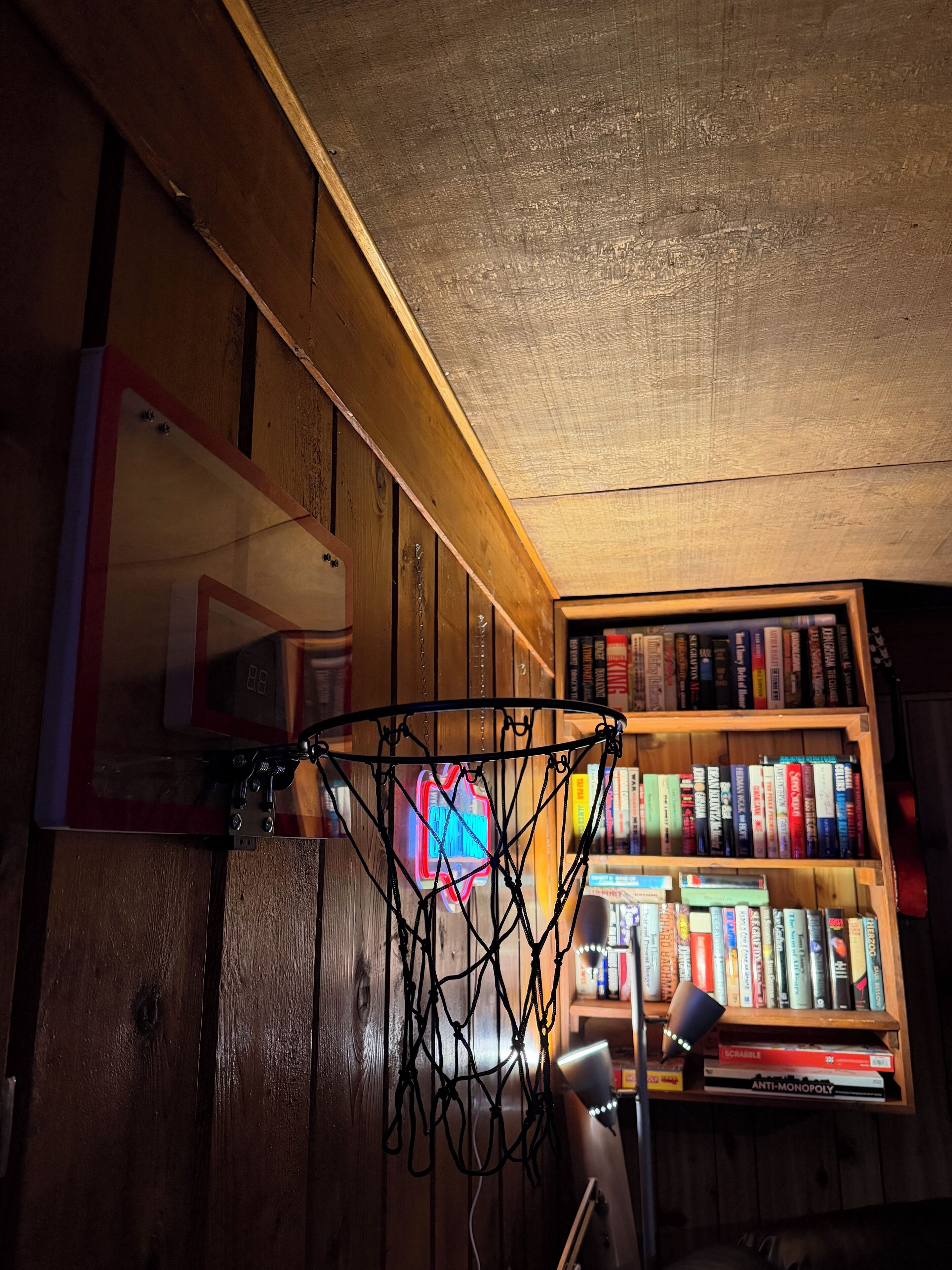 Un panier de basket dans une pièce aux murs en bois, avec une bibliothèque remplie de livres.