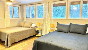 Habitación de hotel con dos camas, una mesita de noche con lámparas y ventanas amplias con cortinas.
