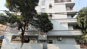 A multi-story building with a white facade, air conditioning units, and a tree in front. - Silver Arrow Guest House  (New Delhi)