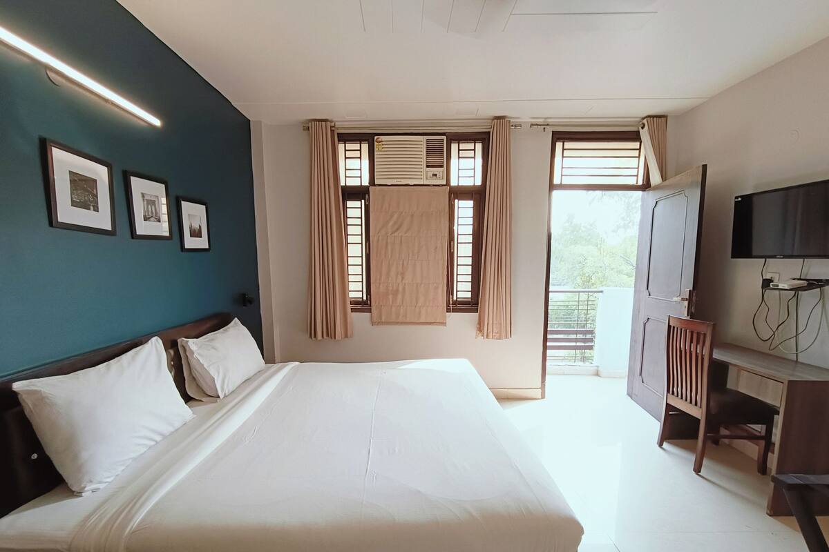 Habitació d'hotel amb un llit gran, una taula de treball amb televisió i un balcó amb cortines.