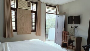 A bedroom with a bed, a desk, a chair, a television, and a window with curtains. - Silver Arrow Guest House  (New Delhi)