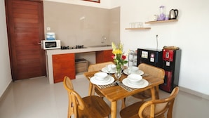 A compact kitchen with a microwave, stove, and refrigerator. There is a dining table set with plates and glasses, and a vase with flowers.