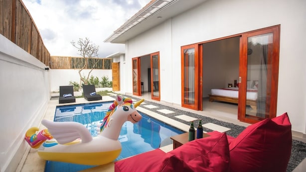 A modern outdoor pool area with a unicorn float, red cushions, and a wooden fence.