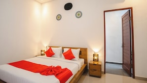 A neatly made bed with a red blanket and pillows, a wooden headboard, bedside lamps, and a door leading to another room.