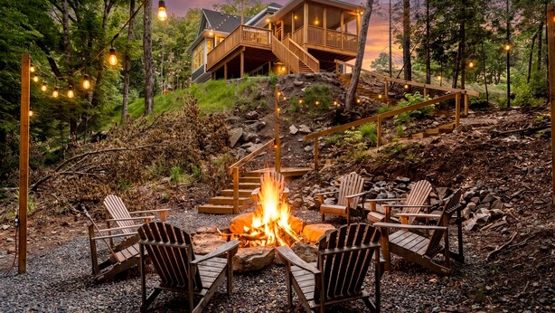 Une cabane avec un foyer et des fauteuils Adirondack, située dans un cadre forestier.