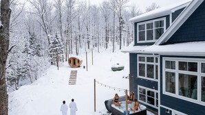 Une maison avec un jacuzzi dans le jardin, entourée d’arbres couverts de neige.
