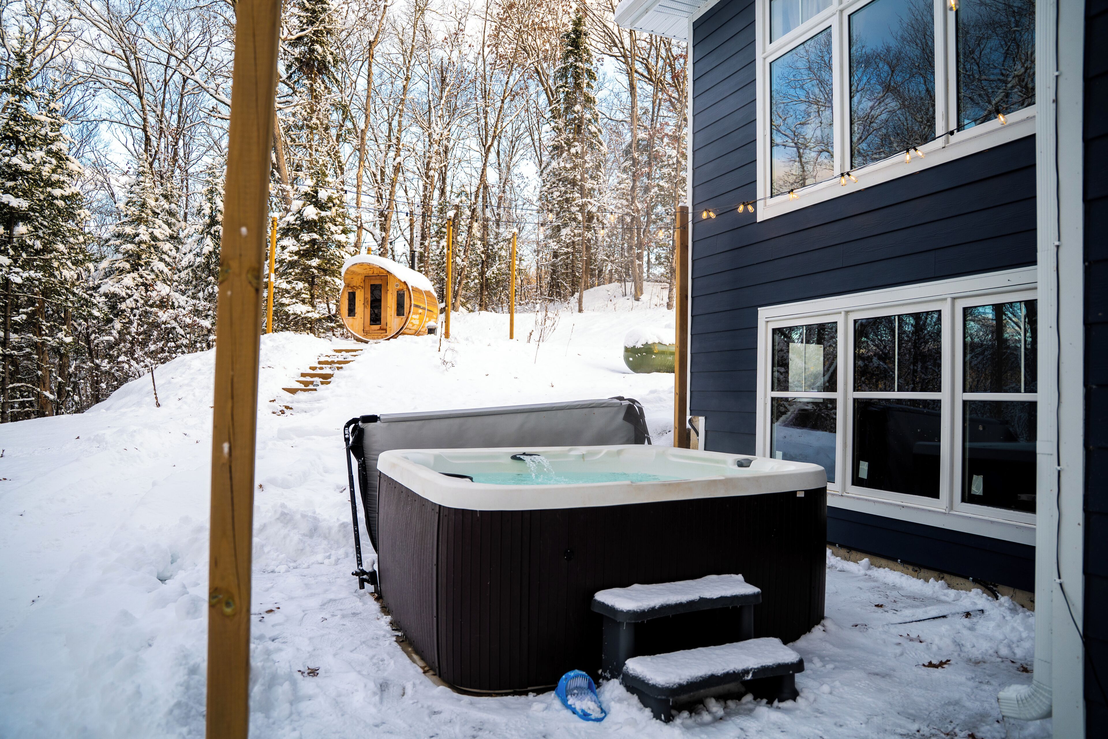 Ein Whirlpool in einer verschneiten Außenanlage mit einer Holzterrasse und Stufen, die zu ihm führen.
