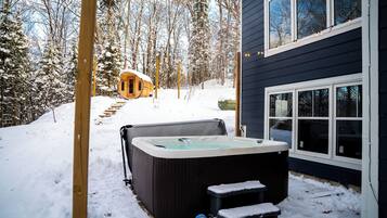Ein Whirlpool in einer verschneiten Außenanlage mit einer Holzterrasse und Stufen, die zu ihm führen.