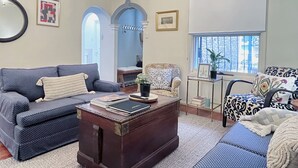 Un salon avec un canapé, un fauteuil et une table basse sur laquelle sont posés des livres. Une fenêtre offre une vue sur l’extérieur.