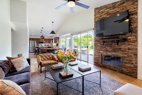 A modern living room with a fireplace, a television, and a dining area in the background.