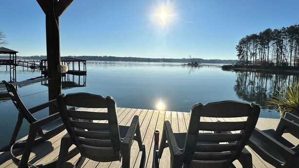 Une terrasse en bois avec deux chaises donnant sur un lac paisible, des allées en bois et un ciel dégagé.