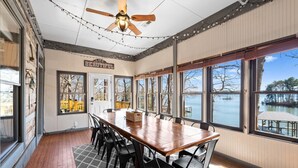Un coin repas avec une table et des chaises en bois, de grandes fenêtres donnant sur un lac et un ventilateur de plafond.