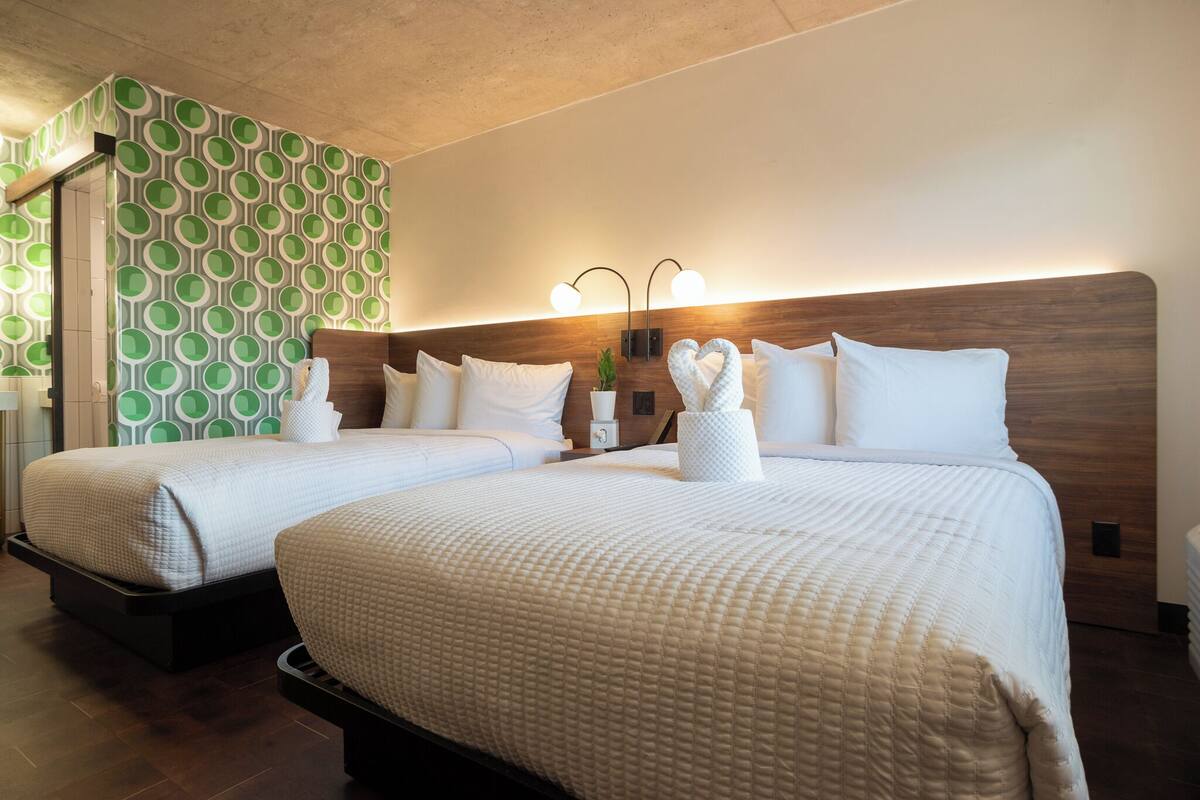 Una habitación de hotel con dos camas, un papel tapiz estampado y un cabecero de madera.