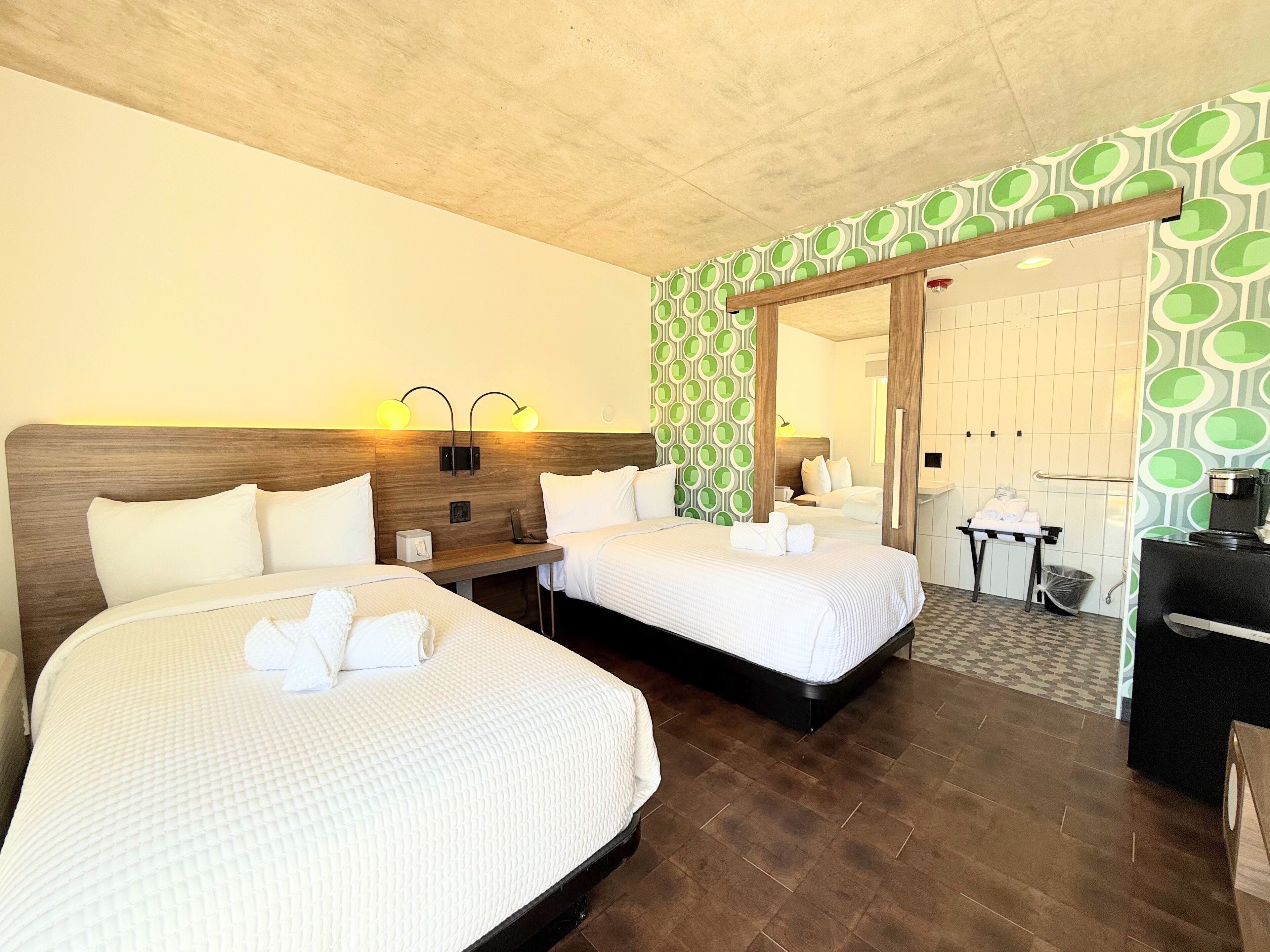 Ein Hotelzimmer mit zwei Betten, einem hölzernen Kopfteil, einem kleinen Nachttisch und einer Wand mit grünem Muster.