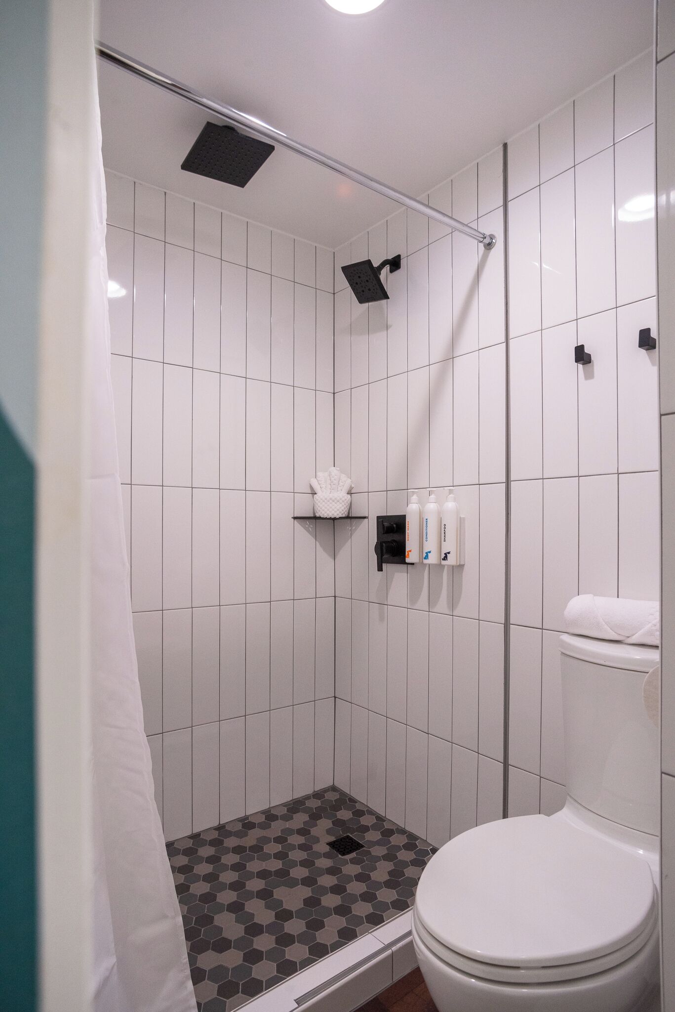 Un baño pequeño con azulejos, ducha, inodoro y un estante con artículos de aseo.