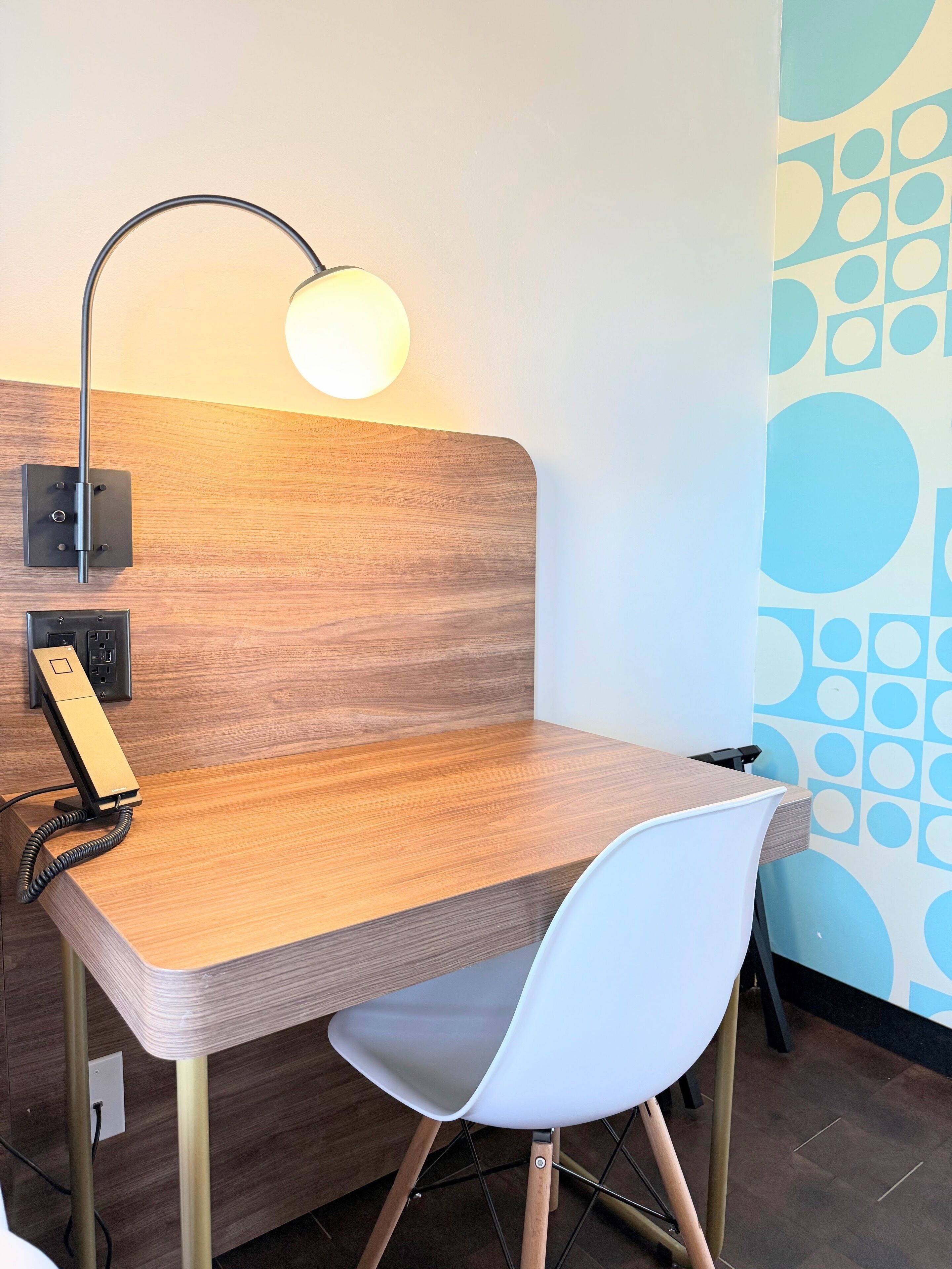 A wooden desk with a white chair, a desk lamp, and a telephone.
