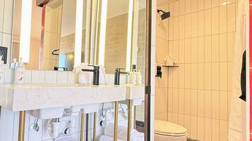 A modern bathroom with a marble vanity, a large mirror, a toilet, and a shower area.