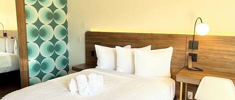 A hotel room with a large bed, a wooden headboard, a bedside table with a lamp, a chair, and a mirror.