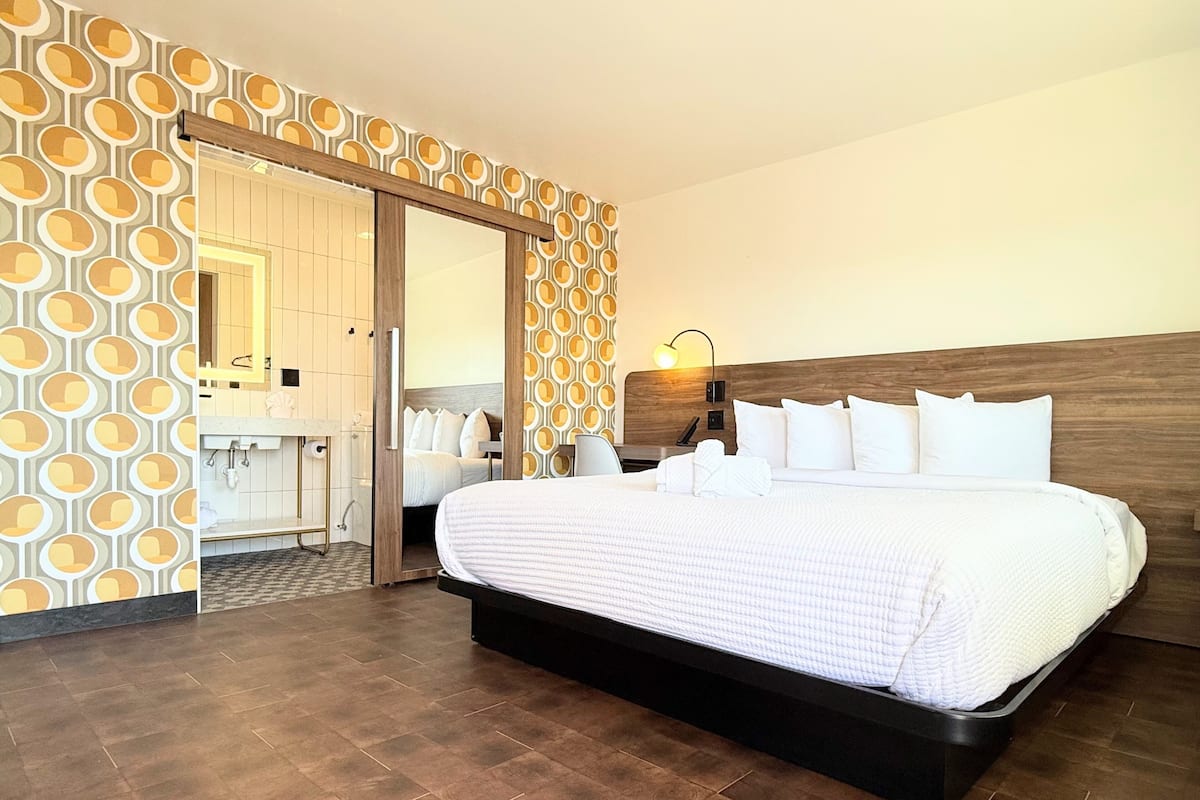 Una habitación de hotel con una cama grande, un cabecero de madera, un espejo y un papel tapiz estampado.