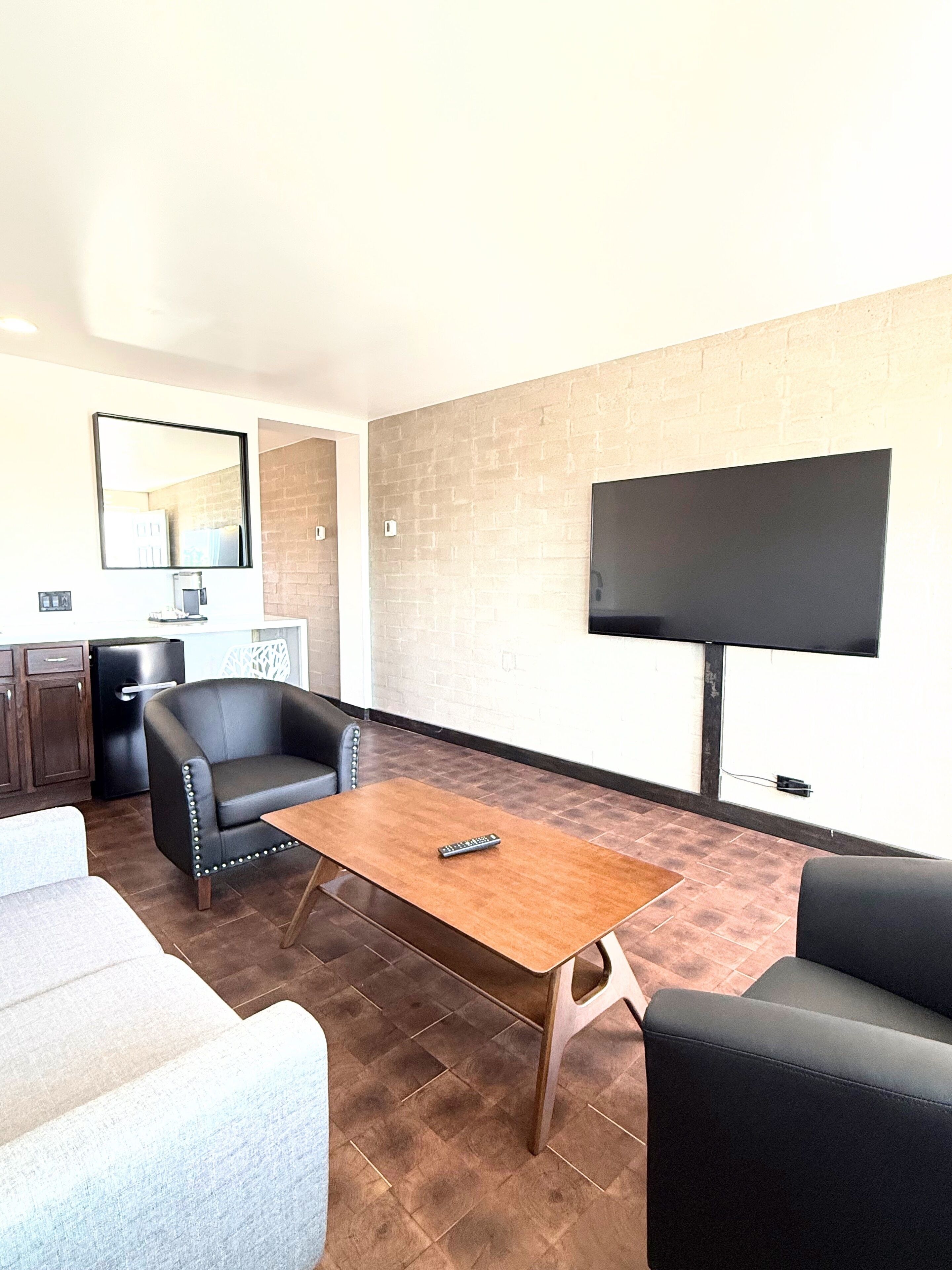 Uma sala de estar moderna com televisão de tela plana, poltronas de couro, mesa de centro de madeira e parede com padrão de tijolos.